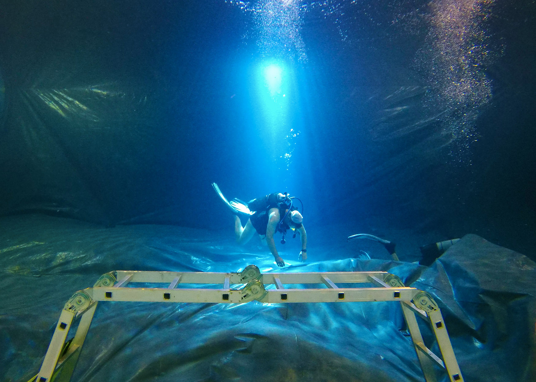 plongeur installe un bâche au fons d'une piscine